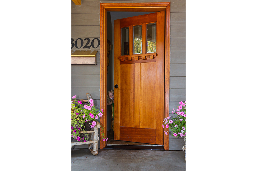 The young girl peeks out of a crack in the front door as she slowly pushes it shut.
